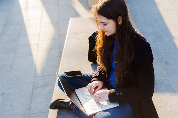 Young woman sitting outdoors enjoys the freedom and flexibiity of Office 365 to keep her in touch with her busy world.