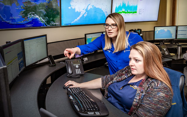 Data-center technicians discussing network performance while viewing several sets of monitors