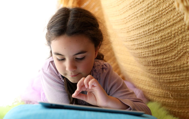 Young girl pokes at her tablet computer while relaxing at home