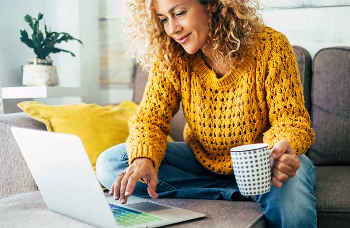 Woman relaxing with a cup of coffee at home while she scans her laptop computer