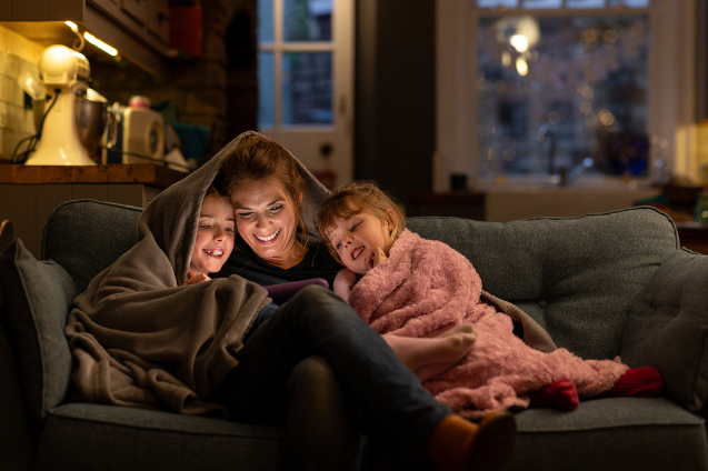 Mom cuddled up with her kids in a blanket, streaming on fiber internet