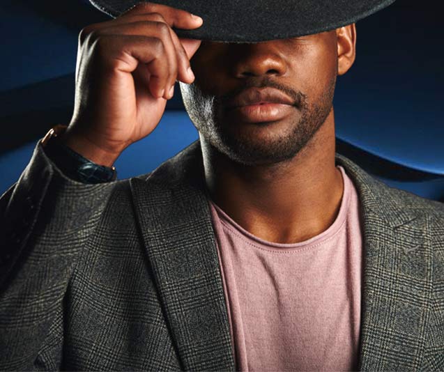 Side lighting washes across the face of a man tipping his hat with eyes hidden