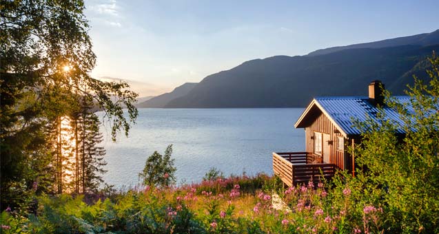 Sunset light baths a lone cabin situated above a large lake with mountain vistas